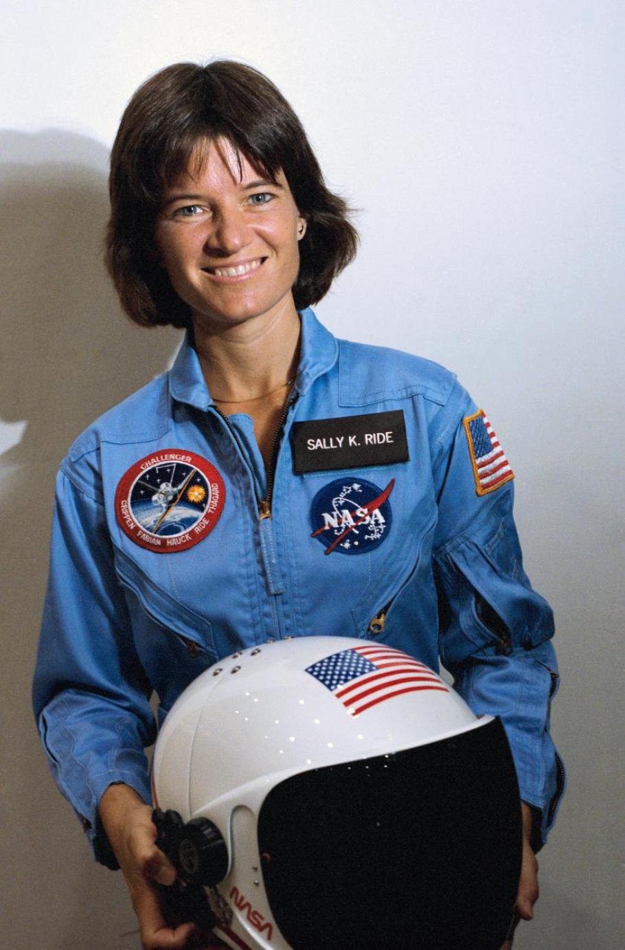 Sally ride in a blue astronaut jumpsuit holding a helmet